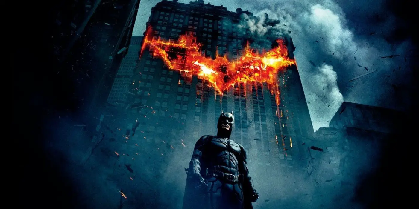 Batman está solo en medio de los escombros de Gotham City con un símbolo de murciélago en llamas en el edificio detrás de él.