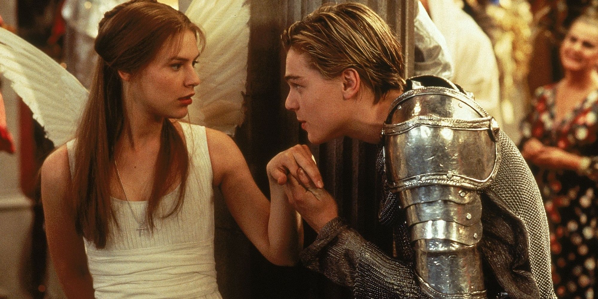 Romeo disfrazado de caballero besando la mano de Julieta, que está disfrazada de ángel.