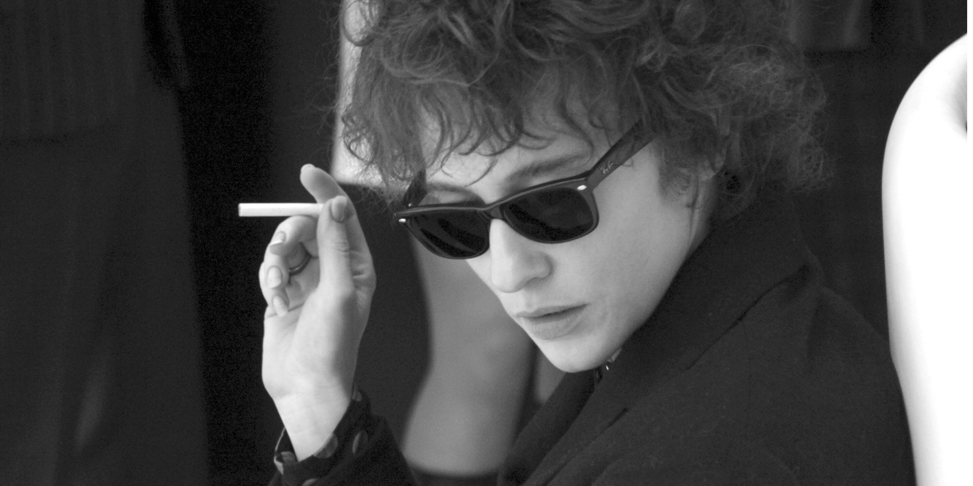 Boby Dylan sosteniendo un cigarrillo y mirando hacia abajo en I'm Not There.