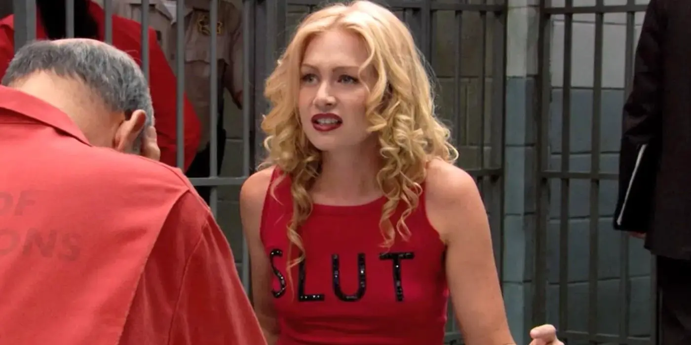 Fotograma de 'Arrested Development': Lindsay Fünke (Portia de Rossi) se sienta en el área de recepción de la prisión luciendo confundida, vistiendo una camiseta roja que dice 'SLUT'.