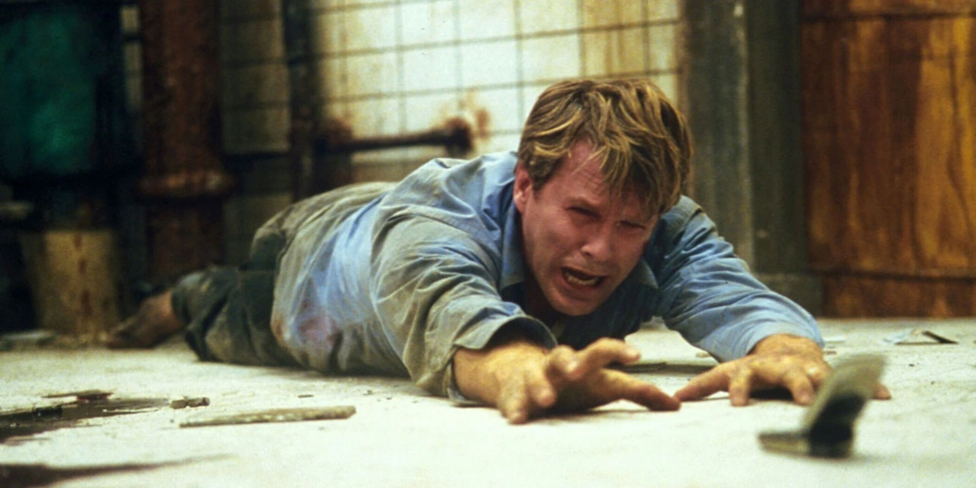 Cary Elwes tirado en el suelo angustiado, alcanzando un teléfono en 'Saw' (2004)