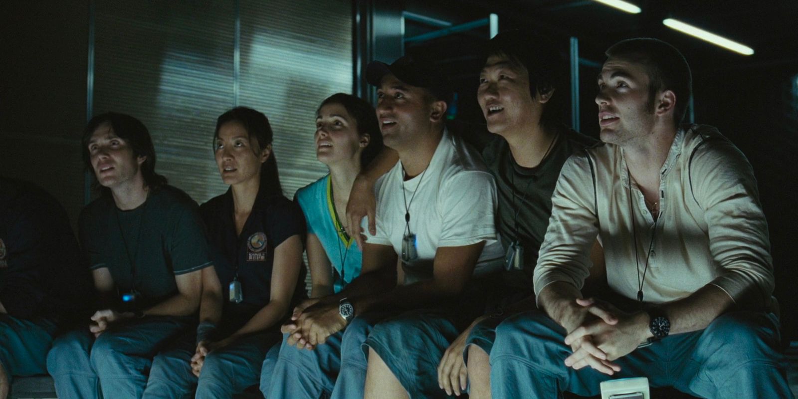 Un equipo de científicos está sentado en una sala de recreación de su nave espacial, sonriendo mientras miran algo juntos.
