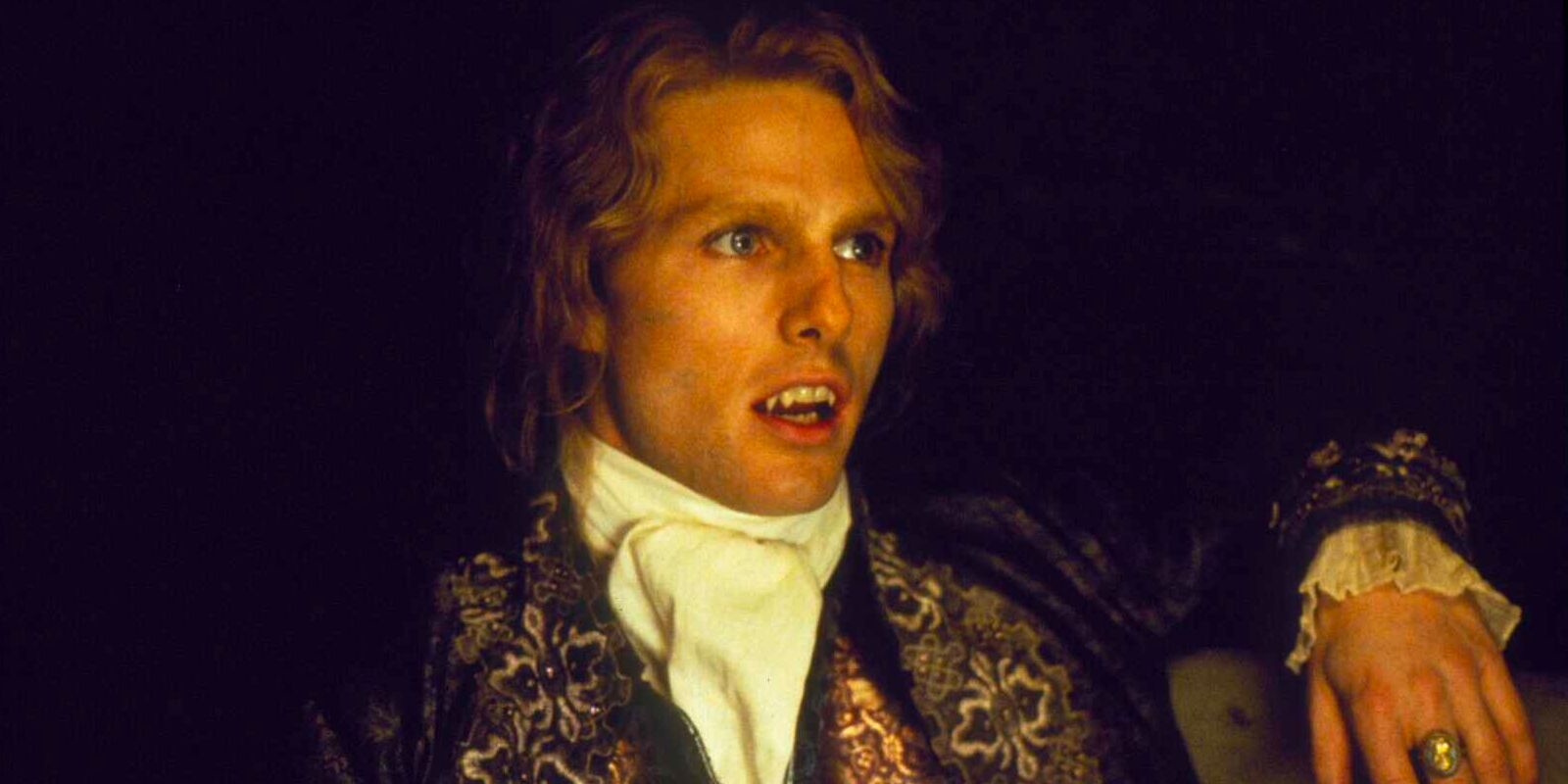 Lestat de Lioncourt, un vampiro centenario, está sentado en una habitación a oscuras y adornado con un elegante atuendo del siglo XVIII.