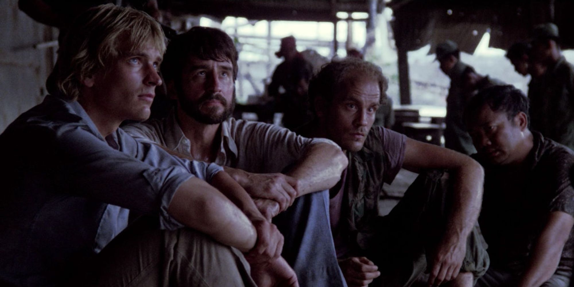 Un grupo de hombres sentados juntos y mirando hacia arriba en 'The Killing Fields'