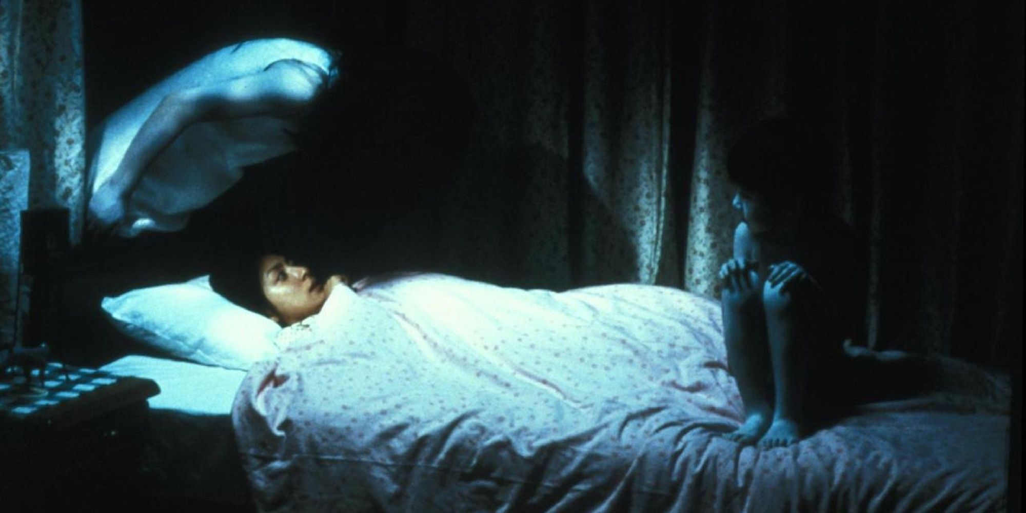 Entidades paranormales sentadas en la cama de Rika en 'Ju-on: The Grudge'.