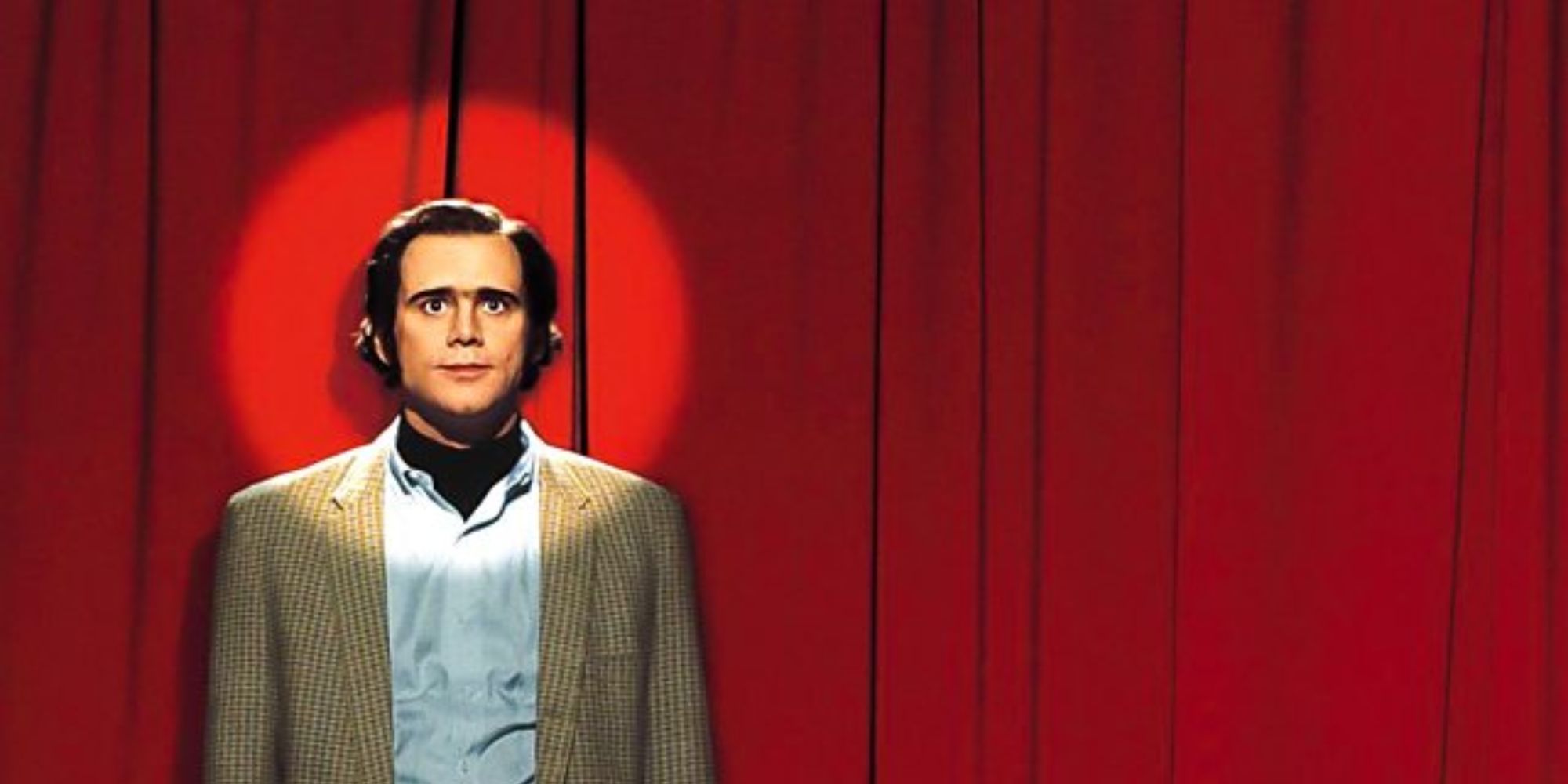 Jim Carrey como Andy Kaufman con un foco brillando sobre él contra una cortina roja en Man on the Moon