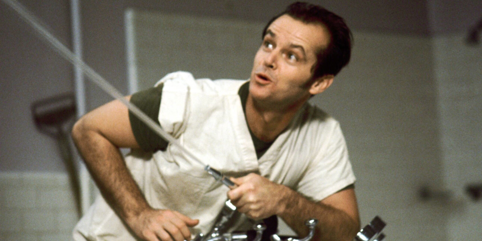 Jack Nicholson como Randle McMurphy apuntando a una fuente de agua a su izquierda en Alguien voló sobre el nido del cuco.
