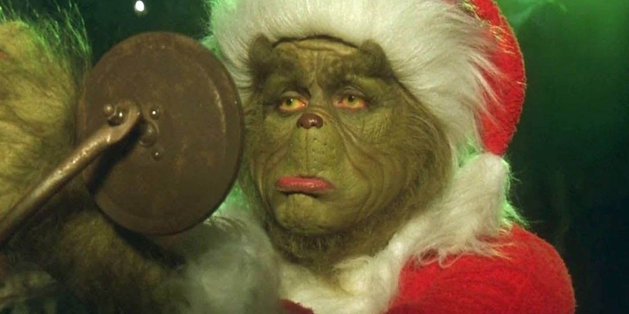 Jim Carrey como el Grinch haciendo pucheros en el espejo lateral de un auto vestido como Santa Claus en Cómo el Grinch robó la Navidad
