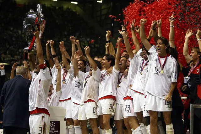 Los jugadores del AC Milan, vestidos con una equipación blanca, levantan el trofeo de la Liga de Campeones mientras cae confeti rojo. 