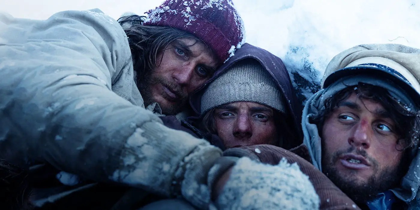 Los supervivientes de un accidente aéreo se acurrucan para calentarse en una imagen fija de La Sociedad de la Nieve. 