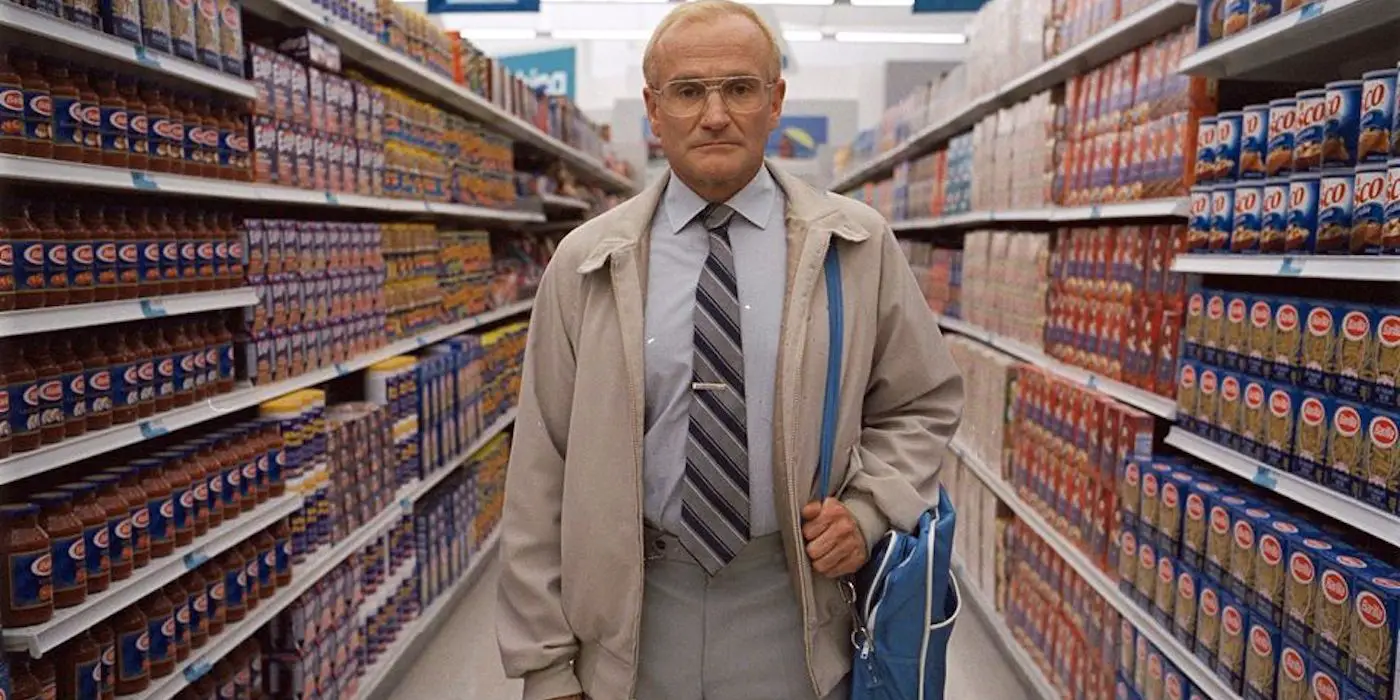 Robin Williams como Sy Parrish, de pie en el pasillo de una tienda de comestibles y mirando fijamente a la cámara en One Hour Photo.