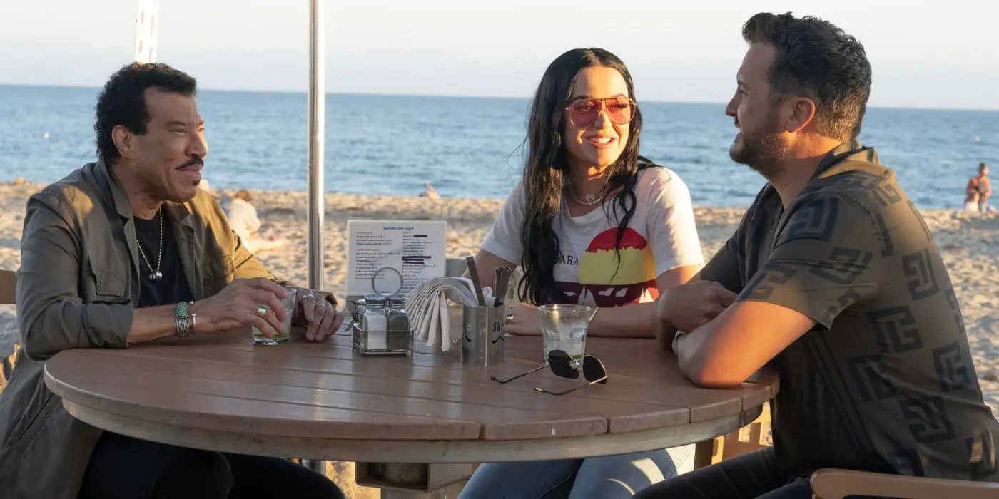 Lionel Richie, Katy Perry y Luke Bryan sentados en una mesa en la playa en la temporada 22 de American Idol.