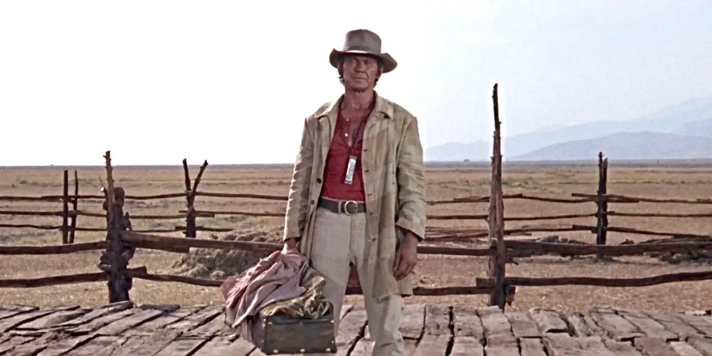 Charles Bronson como Harmonica, usando su armónica y de pie con equipaje en Érase una vez en el Oeste.