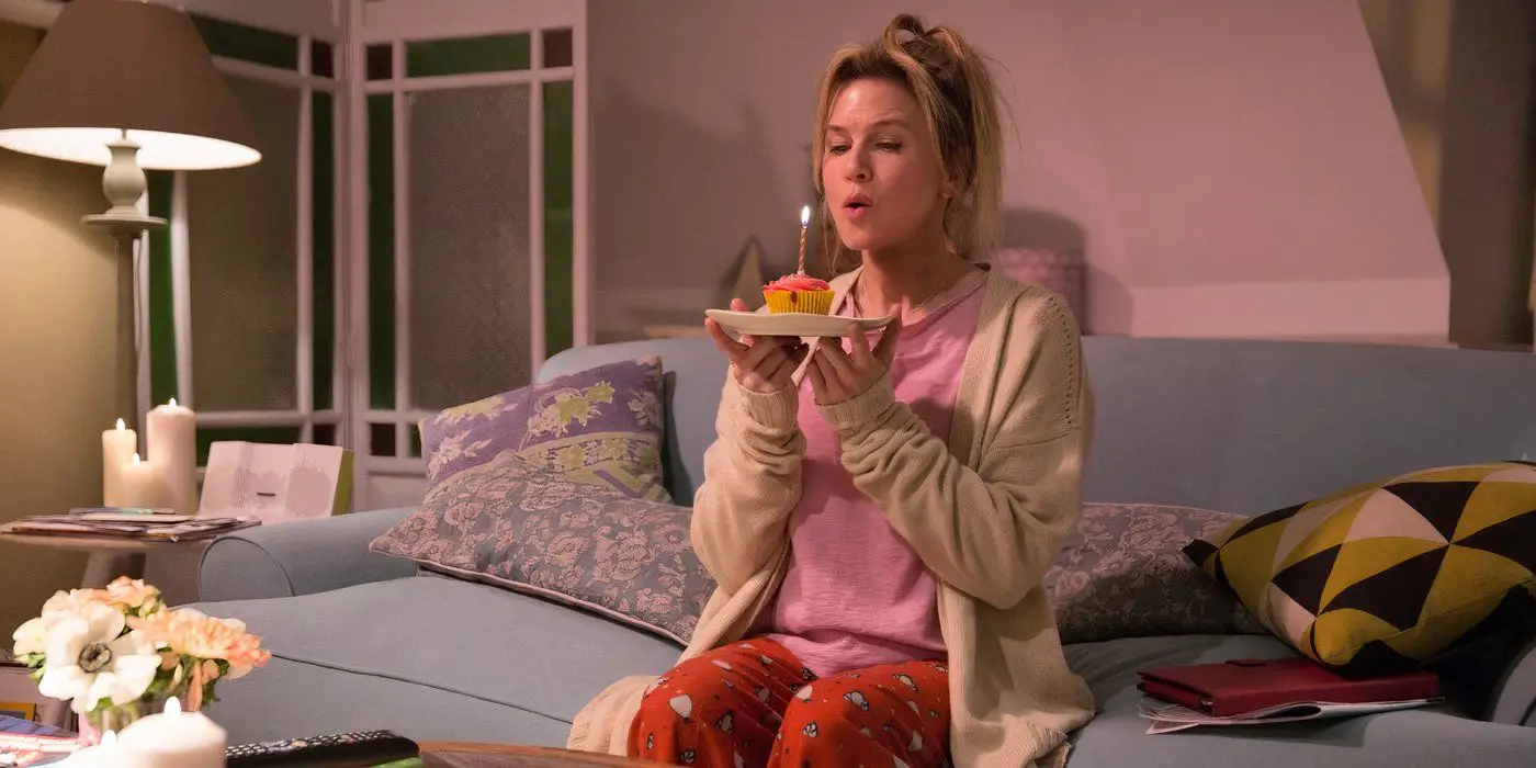 Bridget Jones de Renée Zellweger soplando una vela sobre un cupcake con glaseado rosa.
