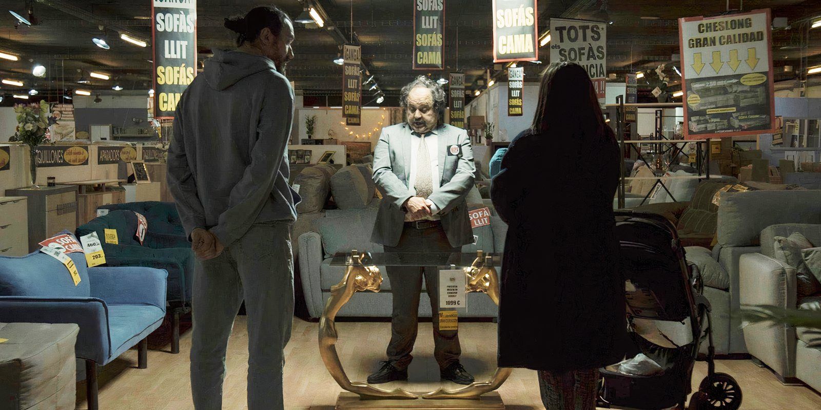 una pareja parada en medio de una tienda de muebles, de espaldas a la cámara, frente a un vendedor que mira una mesa de café ornamentada en The Coffee Table
