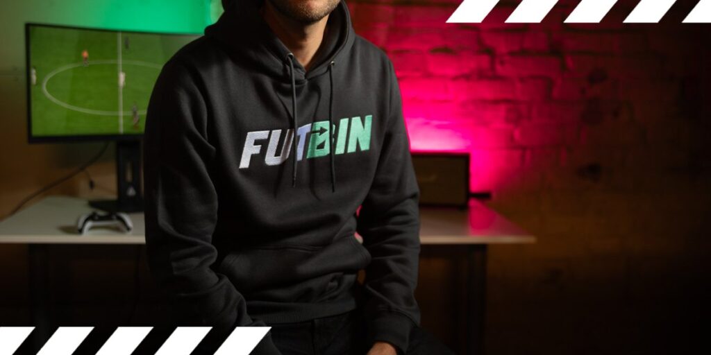 Hombre con sudadera con capucha de futbin con juego EA FC 26 al fondo